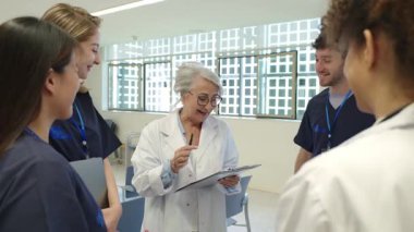 Hastanede tıbbi personelle brifing veren kıdemli doktor, ağır çekimde hasta bakımı ve tedavi stratejilerini tartışıyor.