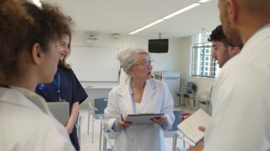 Doktorlar ve hemşireler bir hastane odasında hasta bilgilerini yavaş çekimde gözden geçiriyorlar.