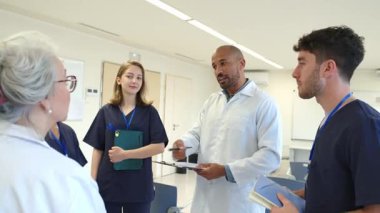 Doktorlar ve hemşireler hasta bilgilerini gözden geçirir, hastane ortamında ortak bir tartışmaya girerler.