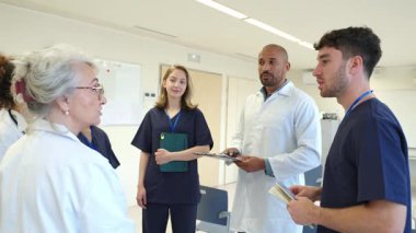 Doktorlar ve hemşireler hastane ortamında hasta bilgilerini ve tedavi planlarını inceliyorlar.