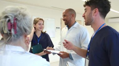 Hastane koridorunda yürürken hasta kayıtlarını inceleyen tıp uzmanları, yavaş çekim profesyonel ortamında sağlık bilgilerini tartışıyor ve işbirliği yapıyorlar.
