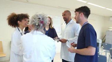 Tıp uzmanları hasta verilerini incelerken hastane koridorunda durup, sağlık hizmetleri bilgilerini analiz ediyorlar.