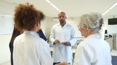 Doktorlar ve hemşireler bir hastane odasında hasta vakaları hakkında tartışıyorlar. Ağır çekimde yakalandılar.