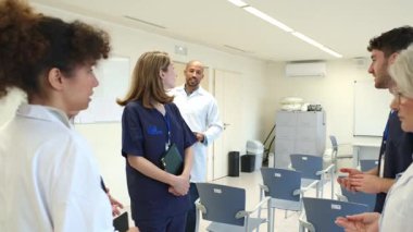 Doktorlar ve hemşireler tıbbi brifinge katılıyor, hasta vakaları hakkında yavaş çekimde fikir alışverişinde bulunuyorlar.