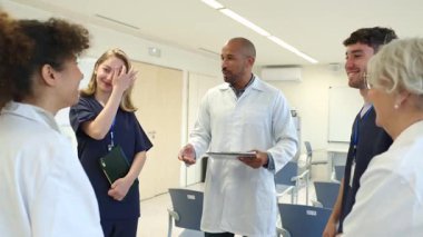 Doktorlar ve hemşireler bir hastane odasında ağır çekimde hastaların tıbbi kayıtlarını tartışıyorlar.