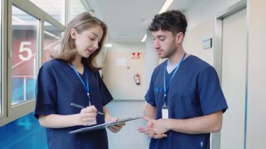 Tıbbi uzmanlar hasta dosyalarını incelerken hastane koridorunda dikilip, odaklanmış uzmanlıkla teşhis ve tedaviyi tartışıyorlar.