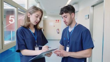 Hastane koridorunda hasta kayıtlarını tartışan tıp uzmanları, yürürken ve sağlık bilgilerini yavaş çekimde incelerken iş birliği yapıyorlar.