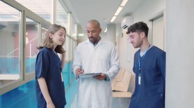 Hastane koridorundaki hasta tıbbi kayıtlarını incelerken iş birliği yapan sağlık uzmanları, yavaş çekimde teşhis ve tedavi stratejilerini tartıştılar.