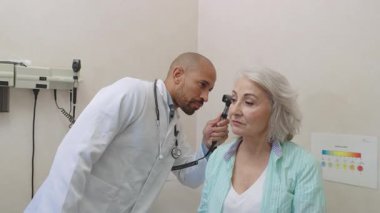 Tıbbi uzman, klinik ortamdaki kapsamlı sağlık kontrolü sırasında otoskopla kıdemli hastaların kulaklarını dikkatlice inceleyerek, ayrıntılı kulak kontrolü ve tanı prosedürüne odaklanır.