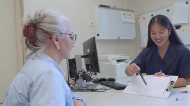 Deneyimli bayan hemşire klinik ortamındaki kıdemli hastalara tıbbi detayları dikkatlice açıklıyor, danışma sırasında profesyonel sağlık hizmetleri iletişimini gösteriyor