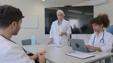 Doktorlar ve hemşireler hastane konferans odasında tıbbi kayıtları inceliyor ve hasta tedavi stratejilerini tartışıyorlar.