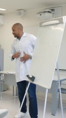 Laboratuvar önlüklü bir doktor, bir sınıf veya hastane ortamında beyaz tahta ve işaretleyici kullanarak tıbbi bir prosedürü açıklıyor. Yavaş çekim