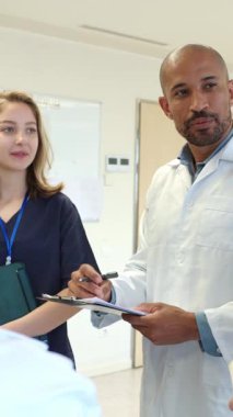 Doktorlar ve hemşireler hastane ortamında işbirliği ve hasta bakımının altını çizerek ağır çekimde tıbbi kayıtları gözden geçirirler.