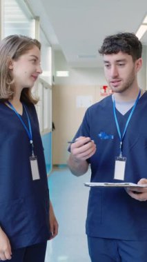 Hastane koridorunda yürüyen hemşireler hasta çizelgeleri ve tedavi planlarını yavaş çekimde tartışıyor.