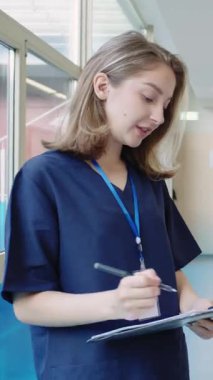 Önlük ve rozet takan genç hemşire not defterine not alıyor ve ağır çekimde bir şey anlatıyor.