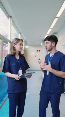 İki sağlık uzmanı, bir kadın hemşire ve bir erkek doktor, bir hastane koridorunda hasta bilgileri hakkında yavaş çekimde tartışırlar.