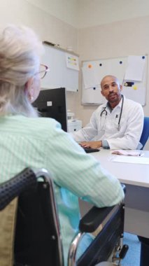 Doktor, tekerlekli sandalyedeki yaşlı kadın hastayla tıbbi geçmişi ve tedavi planı hakkında görüşüyor.