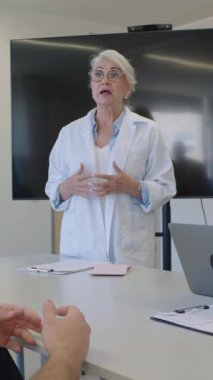 Hastane toplantısı sırasında sağlık hizmetleri ile ilgili görüşler sunan, uzmanlığı yavaş çekimde kendine güvenen davranışlarla paylaşan bir tıp uzmanı.