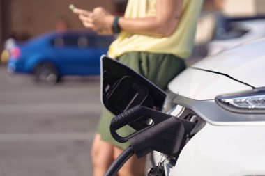 Kamu şarj istasyonunda elektrikli araba şarj eden sürücü, süreci yönetmek için akıllı telefon uygulaması kullanıyor