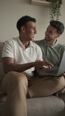 Mutlu eşcinsel çift dizüstü bilgisayar kullanıyor, internette geziniyor, internetten alışveriş yapıyor, tatil için bilet alıyor, bilgi arıyor, video izliyor, haberleri okuyor, çalışıyor veya evde çalışıyor