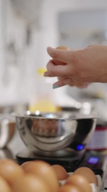 Mutfak terazisine yerleştirilmiş metal bir kâseye yumurta kıran bir kadın.
