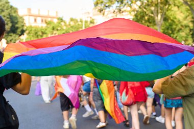 İnsanlar büyük bir gökkuşağı bayrağı taşıyan bir geçit töreninde yürüyorlar, lgbtq haklarını ve toplumu kutluyorlar.