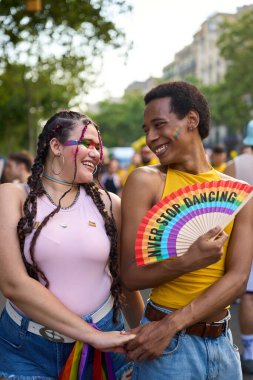 Genç bir çift el ele tutuşuyor ve bir onur etkinliğinde gülümsüyor, lgbtq haklarını ve topluluğunu kutluyorlar.