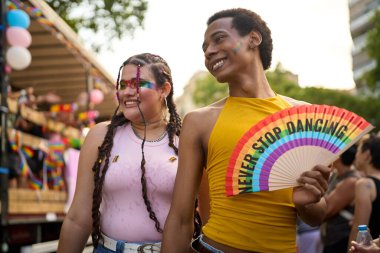 Gurur geçidinde eğlenen iki kişi, elinde gökkuşağı yelpazesiyle dans etmeyi asla bırakmıyor.