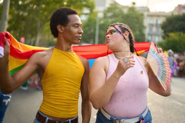 Genç çift canlı bir gurur festivalinde kutlama yapıyor, renkli gökkuşağı makyajı sergiliyor ve bayrak sallıyor, sevgi ve kabulü somutlaştırıyor.