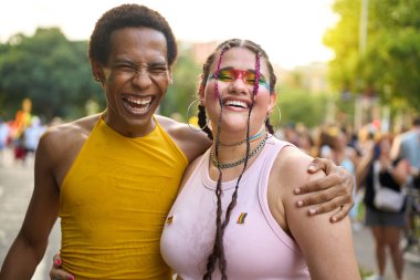 İki arkadaş bir gurur festivalinde gülüyor ve sarılıyorlar, desteklerini ve mutluluklarını gösteriyorlar.