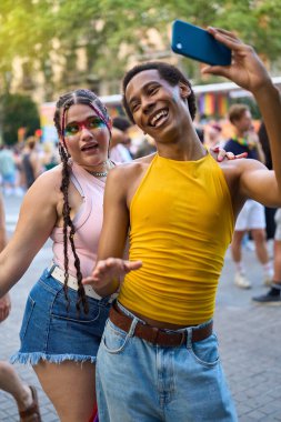 Canlı bir gurur festivalinde gülümseyen ve neşeli bir selfie çeken iki arkadaş, aşkı, çeşitliliği ve lgbtq haklarını birlikte kutluyorlar.