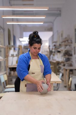 Kadın zanaatkar tezgahında kil şekillendiriyor, küçük işletmesine adanmış rahat bir atölyede eşsiz seramik hazırlıyor.