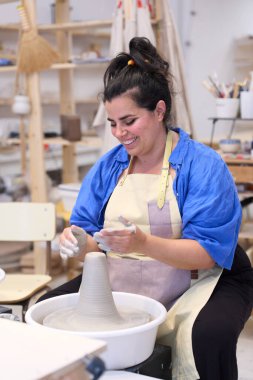 Çömlek çarkında kil hazırlayan dişi çömlekçi, yaratıcılıkla dolu seramik atölyesinde ustalıkla şekil verip şekil veriyor.