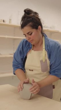 Ham kille çalışan yetenekli bir kadın seramisyen, özenle ahşap tezgahta hammadde yoğururken stüdyo çalışma alanında el yapımı çömlek hazırlıyor.