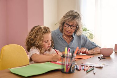 Büyükanne ve torun evde çizim ve el işi yaparken neşeli anları paylaşıyorlar, yaratıcılığı ve bağlantıyı teşvik ediyorlar.
