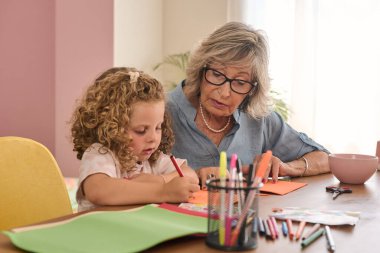 Evde renkli kalemlerle resim çizerken büyükanne ve torun kaynaşıyor, neşeli bir öğleden sonra kahkaha ve yaratıcılıklarını paylaşıyorlar.