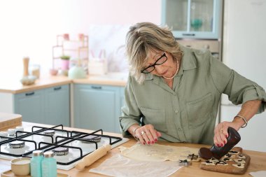 Parlak mutfağında ev yapımı kurabiyeler hazırlarken kurabiye keskisi ve çikolata kullanan yaşlı bir kadın.