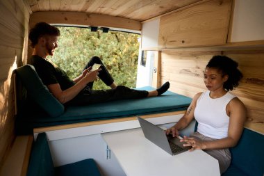 Çok ırklı genç bir çift uzaktan çalışıyor ve karavanda dijital eğlencenin tadını çıkarıyor. Karavan hayatını kucaklıyorlar.