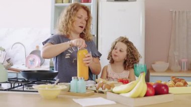 Yavaş çekimde bir annenin, kızı için bir şişe portakal suyu açarken yerel bir mutfakta kahvaltı hazırlarken videosu.