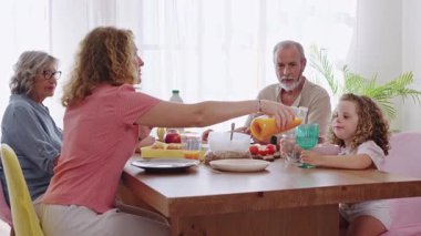 Çok nesilli aile sıcak bir sabah anlarını paylaşıyor. Sıcak mutfak ortamında kahvaltıya bağlanıyor. Yakın aile bağlarını ve besleyici yemekleri temsil ediyor.