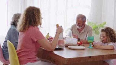Nesiller boyu aile sıcak kahvaltı anlarını paylaşıyor. Huzurlu bir sabah yemeği sırasında mutfak masasında sevgi dolu etkileşimler kuruyorlar.