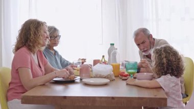 Büyük anne ve büyük baba ve torun evde kahvaltıdan keyif alıyorlar, yavaş çekimde konuşup gülüyorlar.