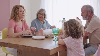 Nesiller boyu aile sıcak kahvaltı anlarını paylaşır, güler yüzlü etkileşimlerle iletişim kurar ve güneşli mutfakta birlikte sabah yemeğinin tadını çıkarır.