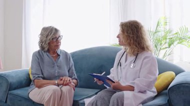 Kadın doktor evde yaşlı bir hastayla görüşüyor, not alıyor, yavaş çekim videosu var.