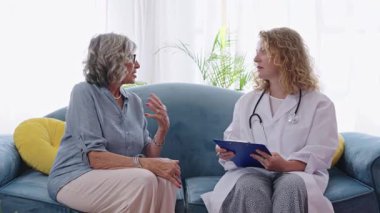 Tecrübeli bayan doktor dikkatlice dinlerken, üst düzey kadın oturma odasının penceresinin yanındaki şefkat dolu tıbbi konsültasyon sırasında sağlık sorunlarını anlatıyor.