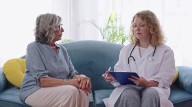 Sağlık uzmanı ev ziyareti sırasında semptomları tarif eden yaşlı kadını dinlerken not alıyor.