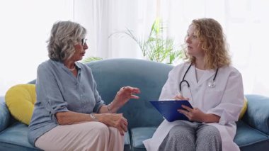 Profesyonel sağlık hizmeti sağlayıcısı, ev danışmanlığı sırasında tıbbi belirtileri açıklayan, güven ve empati ileten kıdemli hastayı dikkatle dinliyor.