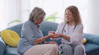 Yaşlı bir hastaya ilaç dozajını açıklayan kadın doktor koltukta ağır çekimde oturuyor.