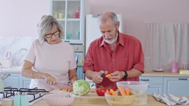 Kıdemli çift havuç soyup doğruyor ve diğer sebzeleri parlak bir mutfakta yavaş çekimde yakalıyorlar.