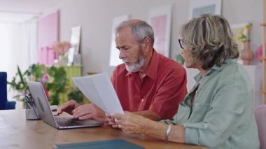 Yaşlı çift evrakları inceliyor ve bilgisayar kullanıyor. Yavaş çekimde bilgiyi tartışıyor ve analiz ediyor.